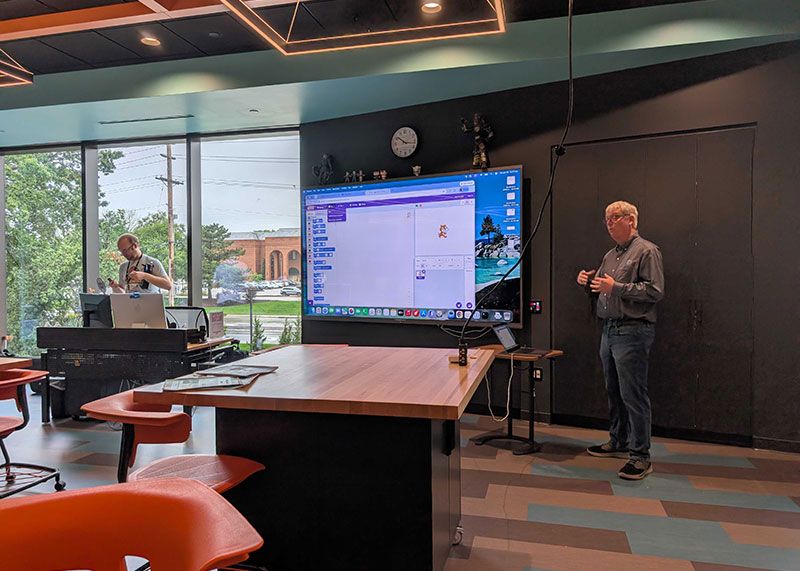 A Unity Foundation volunteer presenting a Scratch programming project on a large display to campers in the library technology room.