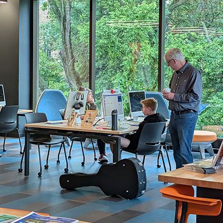 Campers at workstations in the Clark Family Branch learning room, with a volunteer moving between them.